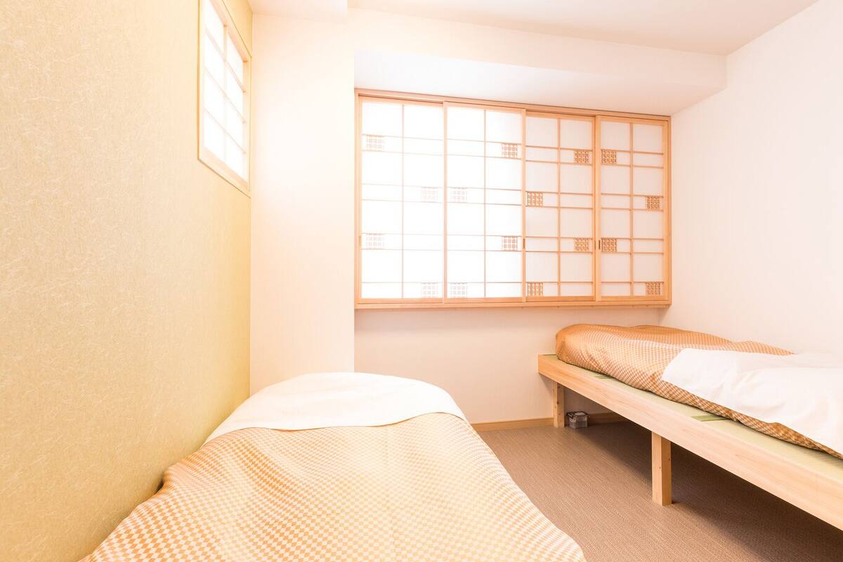Una habitación con dos camas individuales, un panel corredero estilo shoji y un ventanal pequeño.