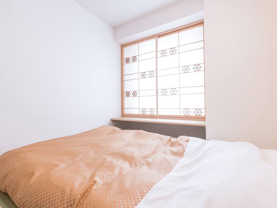 Una camera da letto con un letto, una finestra con motivo geometrico e una parete semplice.