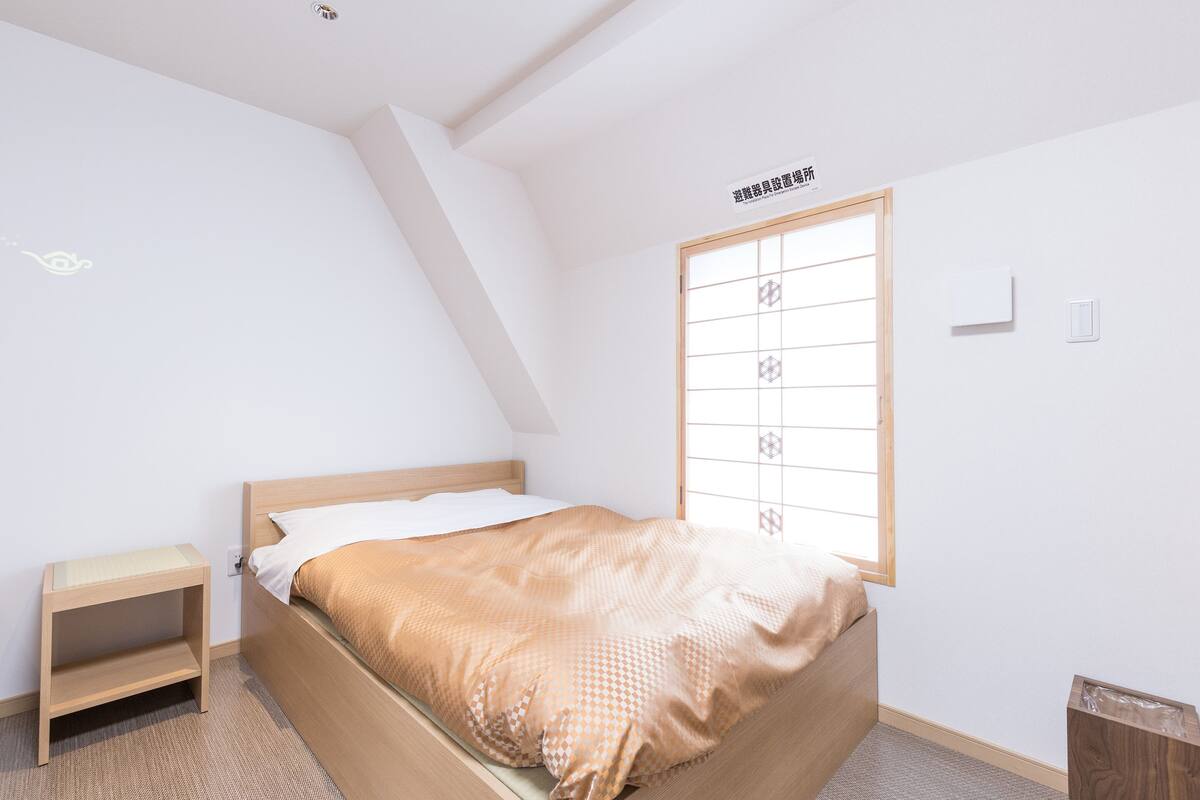 Un dormitorio con cama, mesita de noche, ventana con vistas y lámpara en el techo.