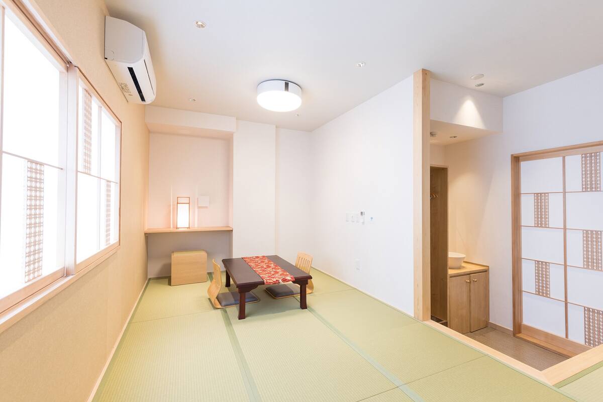 Una habitación japonesa tradicional con suelo de tatami, una mesa baja con un tapete rojo, puertas correderas y un aire acondicionado instalado en el techo.