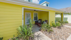 A yellow house with a covered porch, a door marked '18', and a small garden with plants.