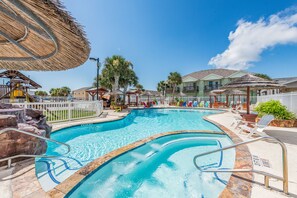 A swimming pool with a stone border, lounge chairs, and a thatched umbrella.