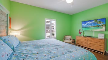 Un dormitorio con cama, cómoda, silla, televisor y ventana con vista a la playa.