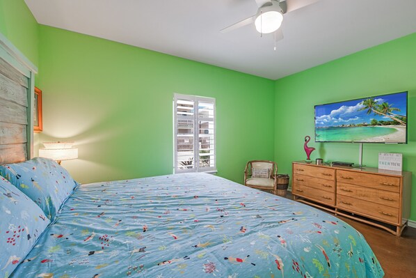 Ein Schlafzimmer mit Bett, Kommode, Sessel, Fenster und Fernseher an der Wand.