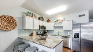 A modern kitchen with white cabinetry, a granite countertop, a stainless steel refrigerator, and a built-in island with bar stools.