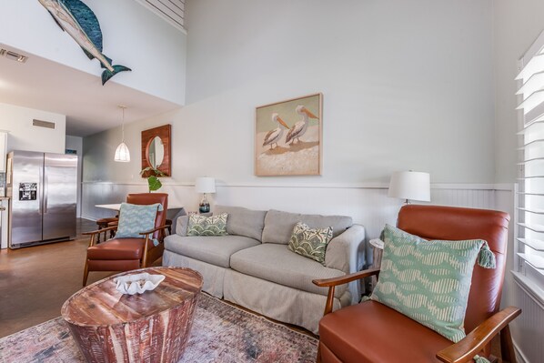 Un vaste espace de vie comprenant un canapé, des fauteuils, une table basse et un tableau représentant des oiseaux, accroché au mur.