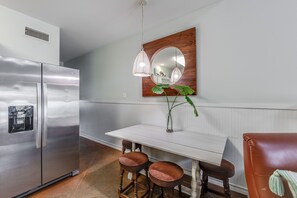 A modern kitchen with a stainless steel refrigerator, a white dining table with two wooden stools, and a mirror with a wooden frame.
