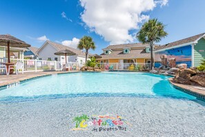 A swimming pool with a tropical theme, surrounded by colorful buildings and palm trees.