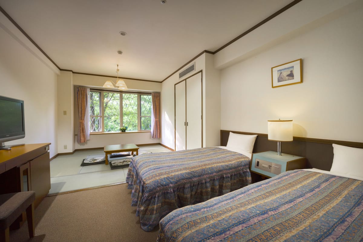 A hotel room with two beds, a desk, a television, and a window with curtains.