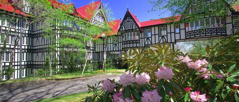 A traditional half-timbered building with a red roof, surrounded by lush greenery and flowering plants.