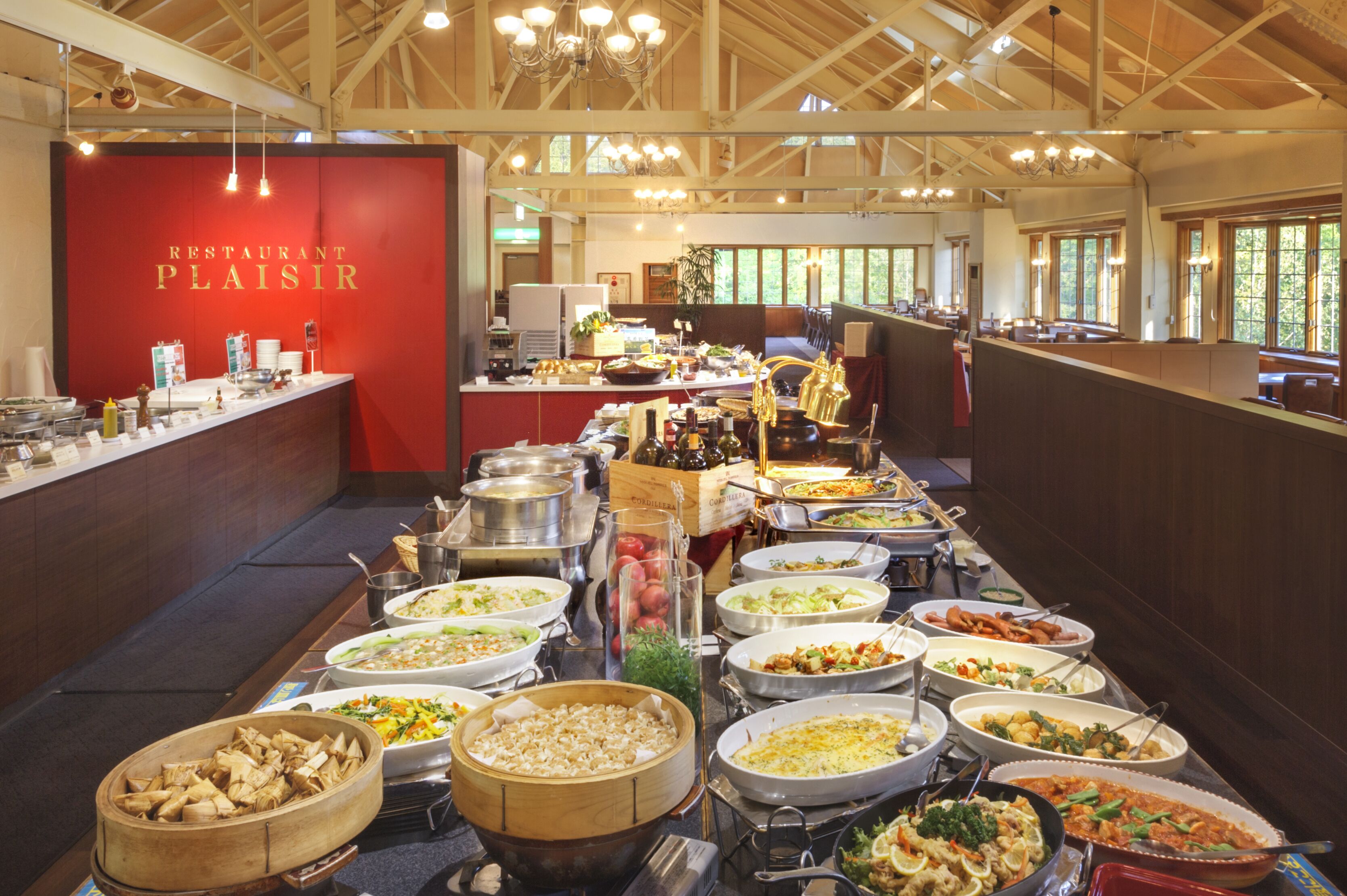 Buffet montado num restaurante, com diversos pratos e uma parede vermelha com o nome do restaurante.