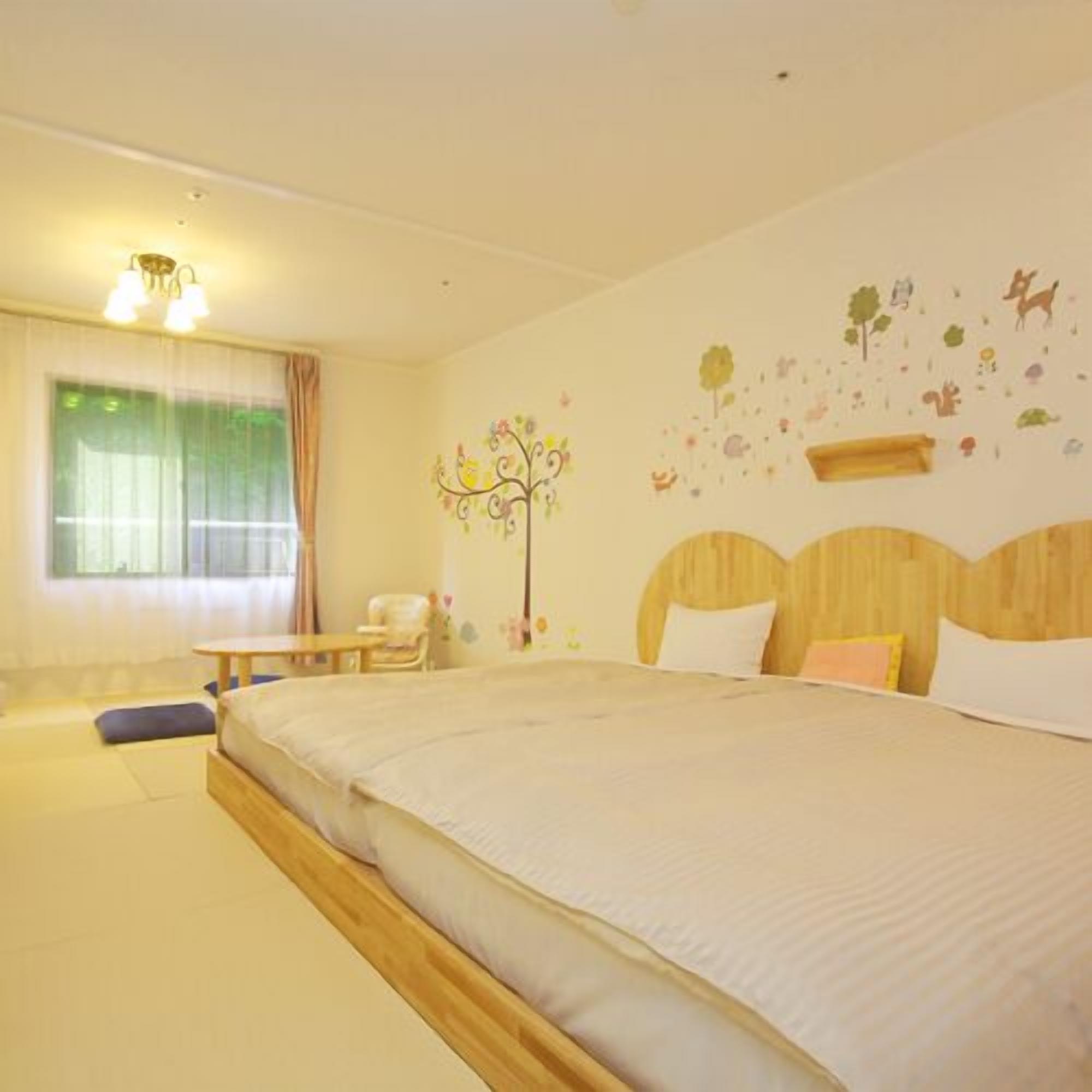 A bedroom with a large bed, a chair, a small table, and a decorative wall mural.