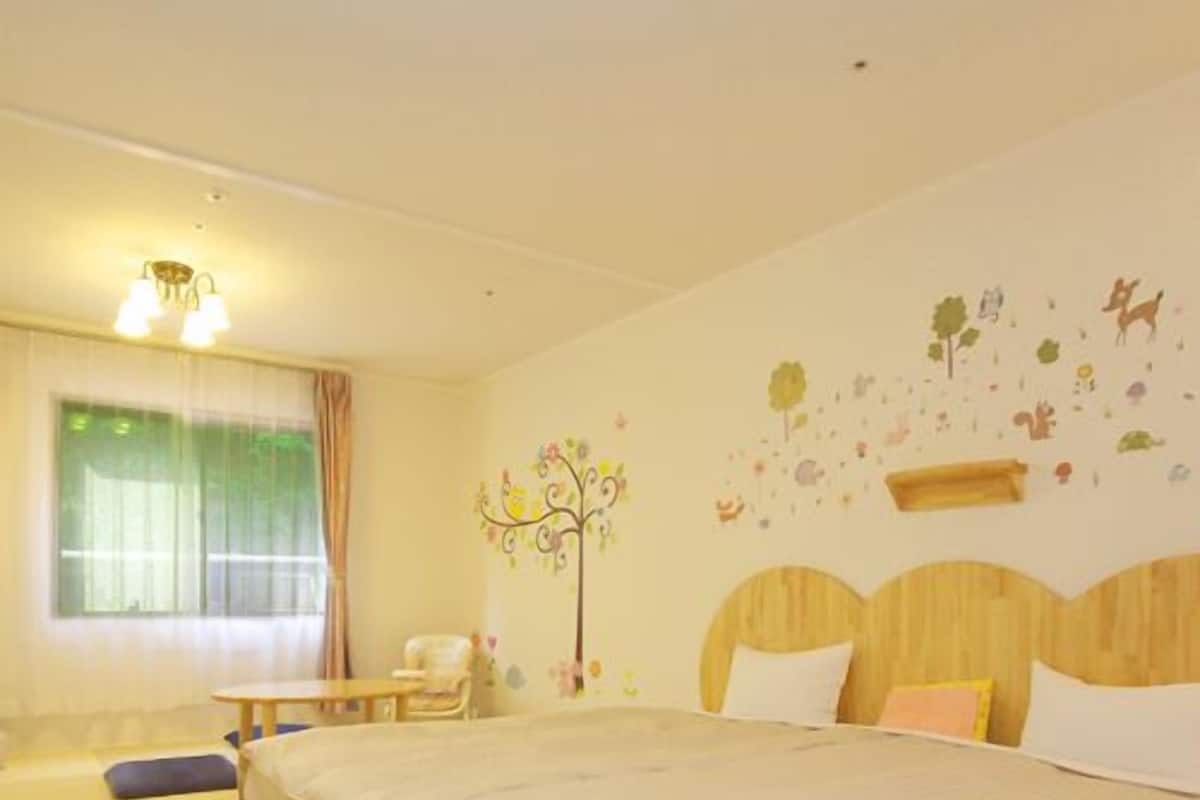 A bedroom with a large bed, a chair, a small table, and a decorative wall mural.