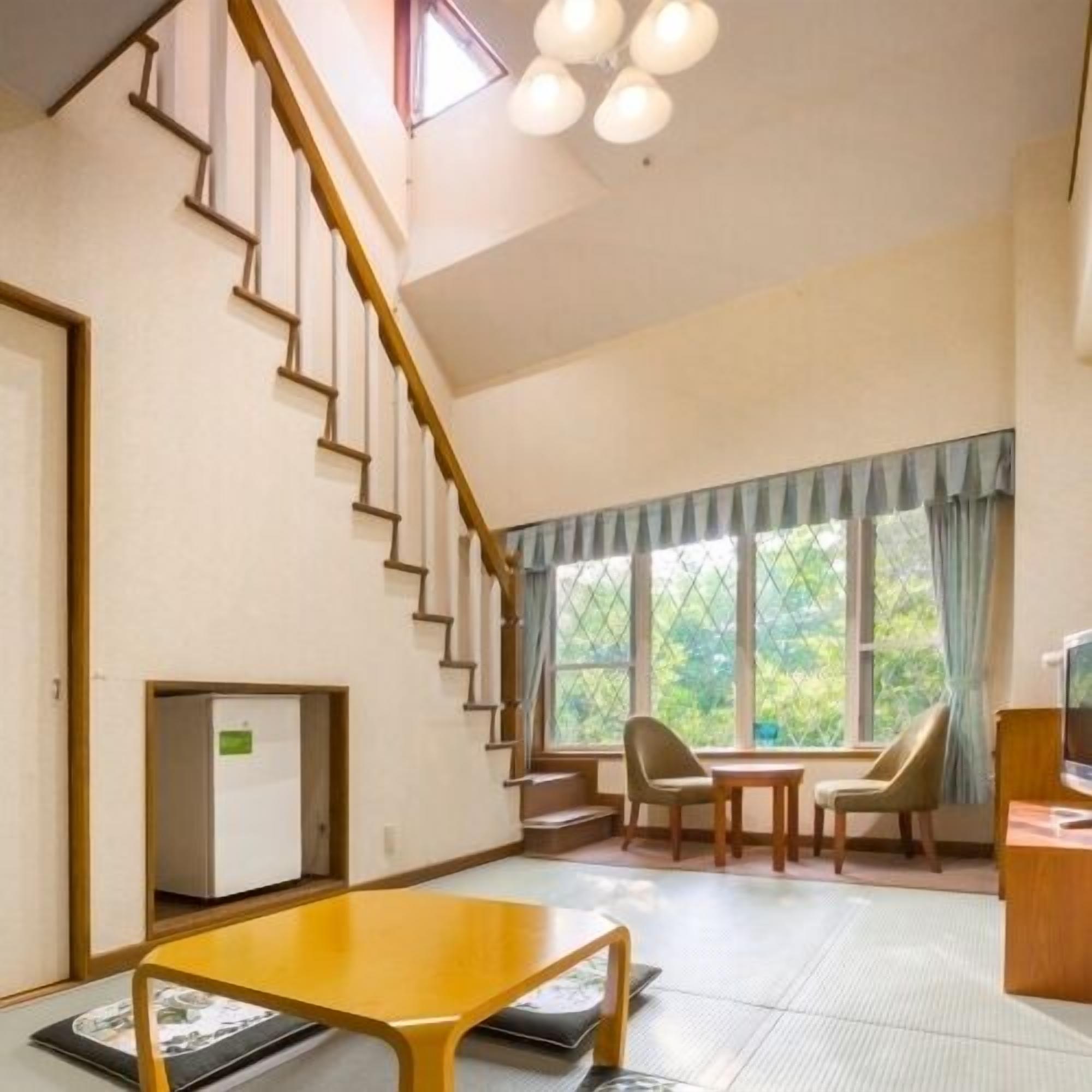 A room with a staircase, a dining area with chairs, a table, and a television.