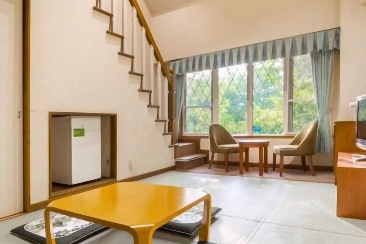 A room with a staircase, a dining area with chairs, a table, and a television.