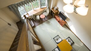 Een kamer met hoge plafonds, een eethoek, een kleine tafel en een bank.