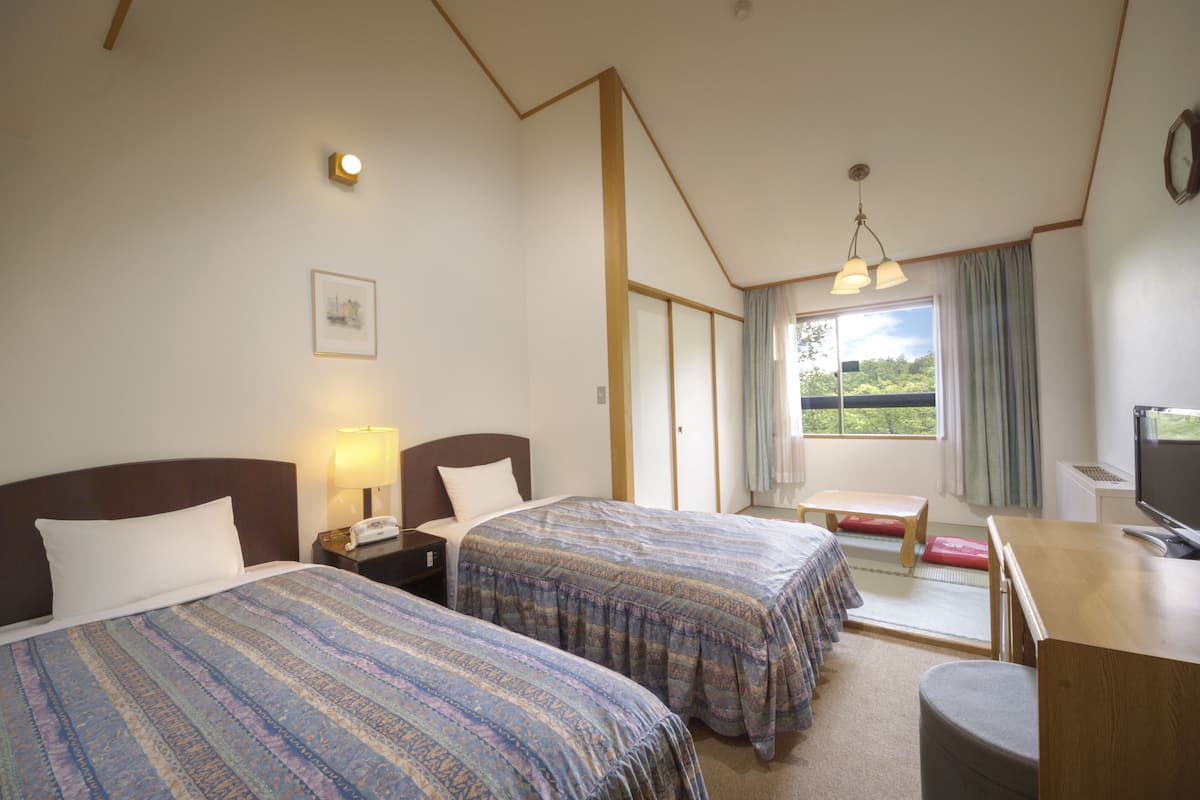 A hotel room with two beds, a desk, a TV, and a window with a view.