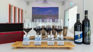 Een proefruimte met wijnglazen op een houten plank, een fles 1837 Barossa wijn, en een wijnkoeler.