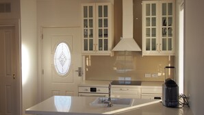 Een keuken met witte kasten, een centraal keukenblok met een spoelbak, en een rvs afzuigkap.