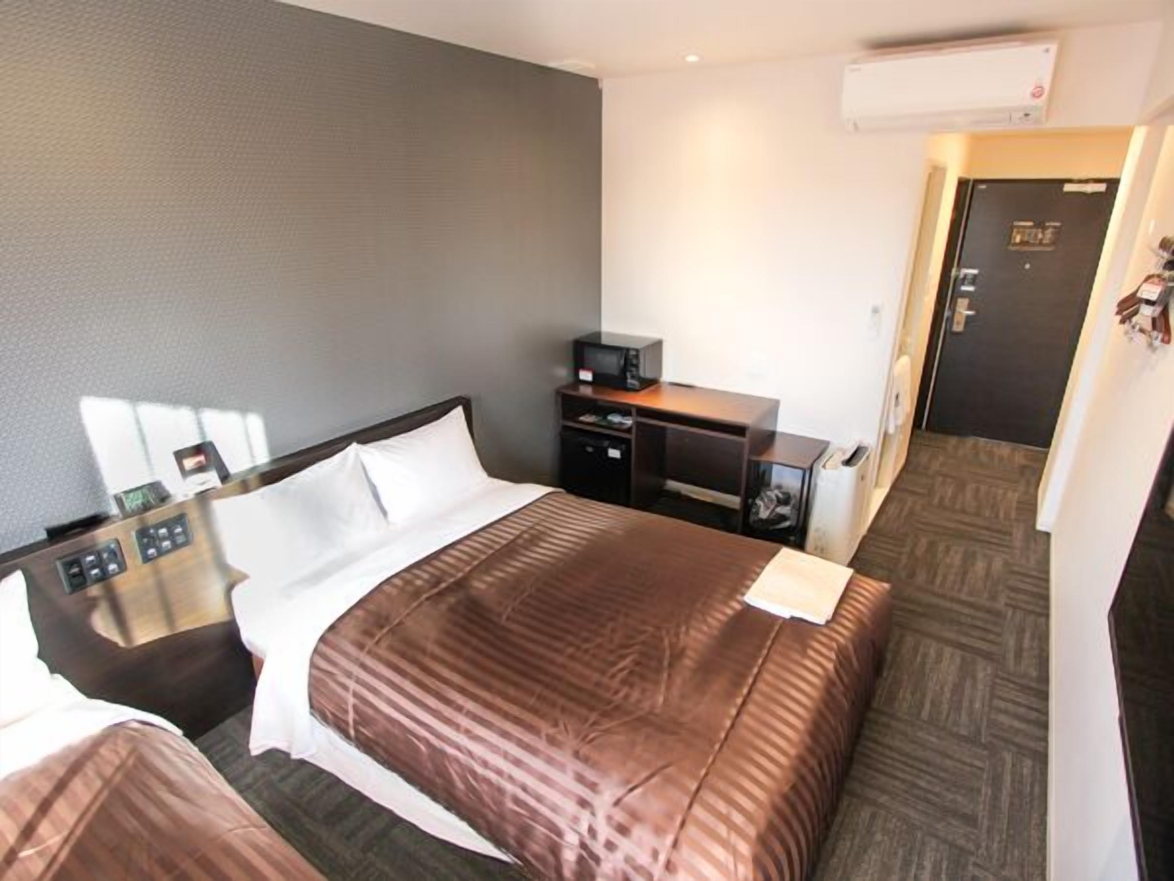 Habitación de hotel con cama, mesitas de noche, escritorio, silla, armario y aire acondicionado.