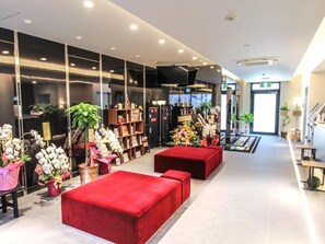 A modern hotel lobby with red seating, a reception desk, and a large window displaying a cityscape. - Hotel Livemax Osaka Kadoma (Kadoma)