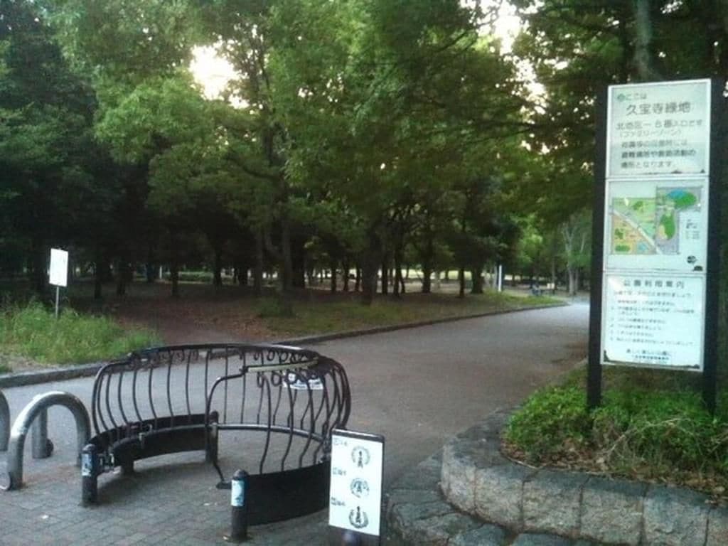 A park entrance with a curved metal bench, a map sign, and a stone planter.