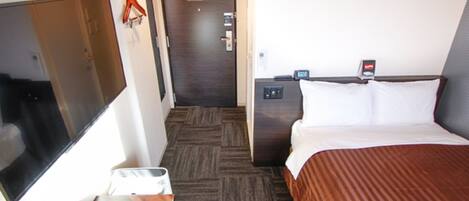 A hotel room with a bed, a TV, a desk with a chair, a door, and a wall-mounted phone.