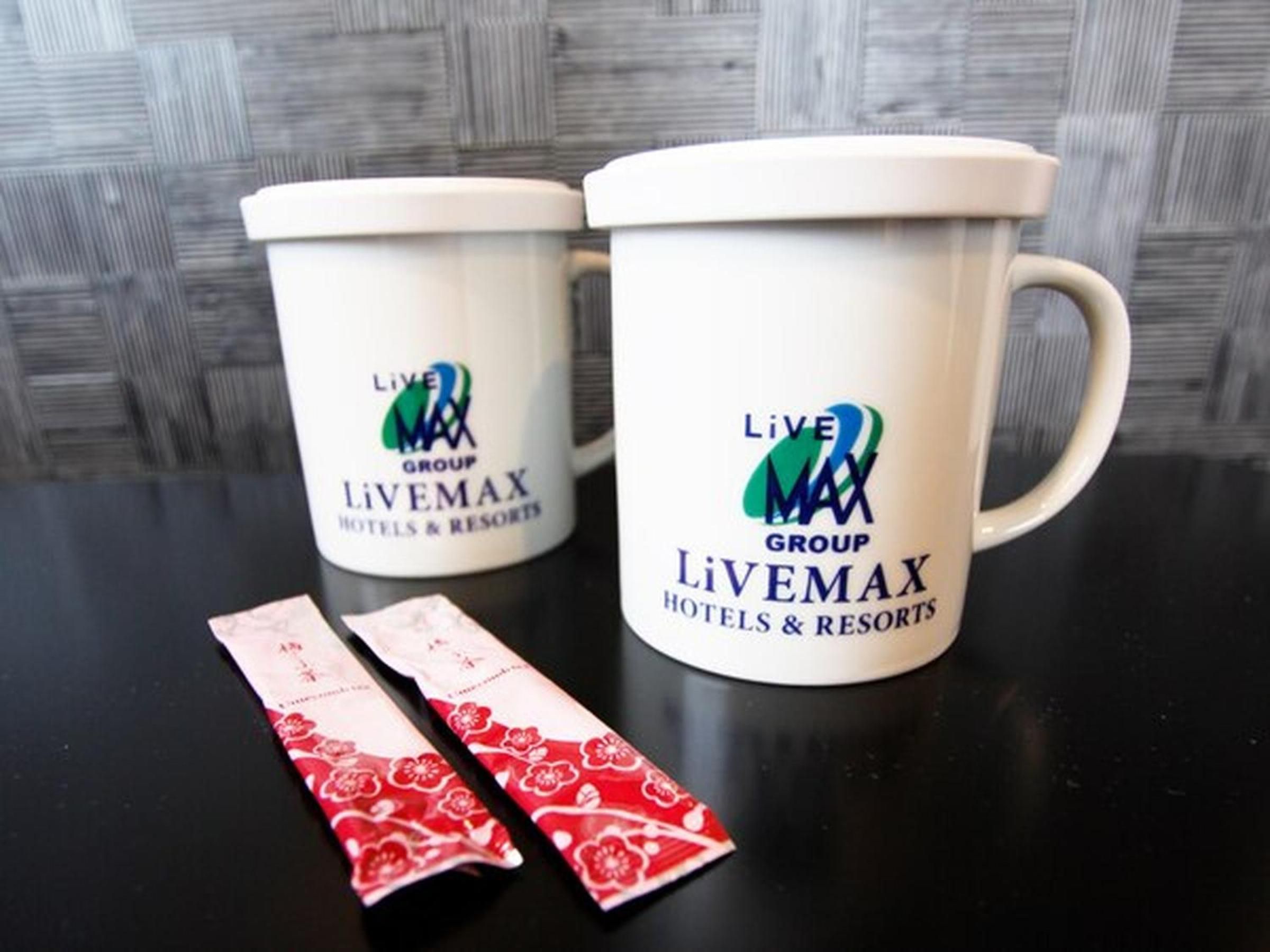 Two white mugs with the Live Max Group Livemax Hotels & Resorts logo, and two red and white tissue packets on a black surface.