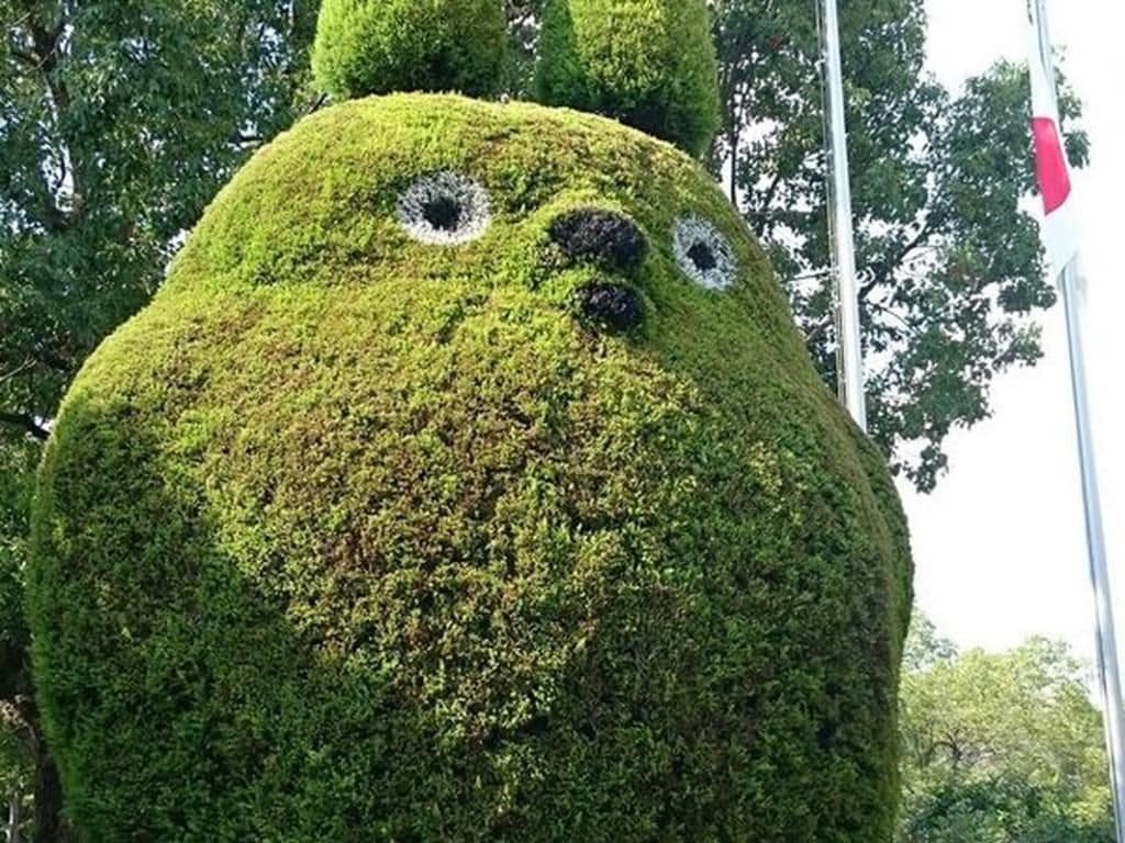 A spherical topiary with a face, surrounded by trees.