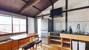 A compact kitchen with wooden flooring, a dining area with a bench, a refrigerator, and a window with a view of buildings. - Seven Stay Ouchi (Kyoto)