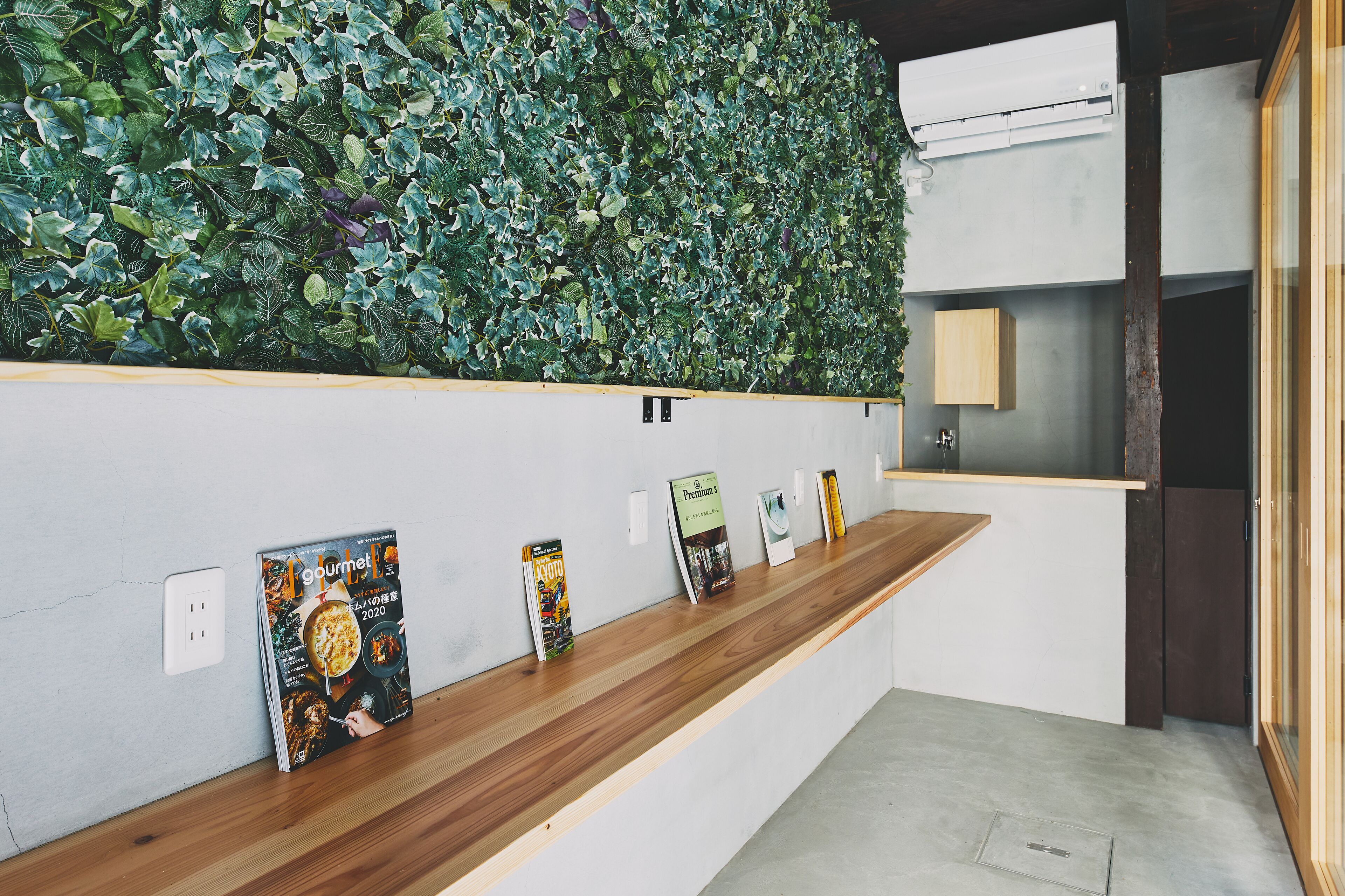 Un espace d’accueil avec un comptoir en bois, des magazines et un mur végétal.