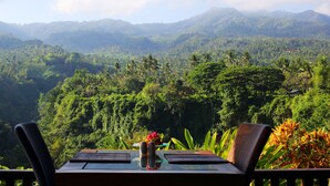 A table with chairs and a vase of flowers, overlooking a lush, mountainous landscape. - Shanti Natural Panorama View Hotel (Sukasada)