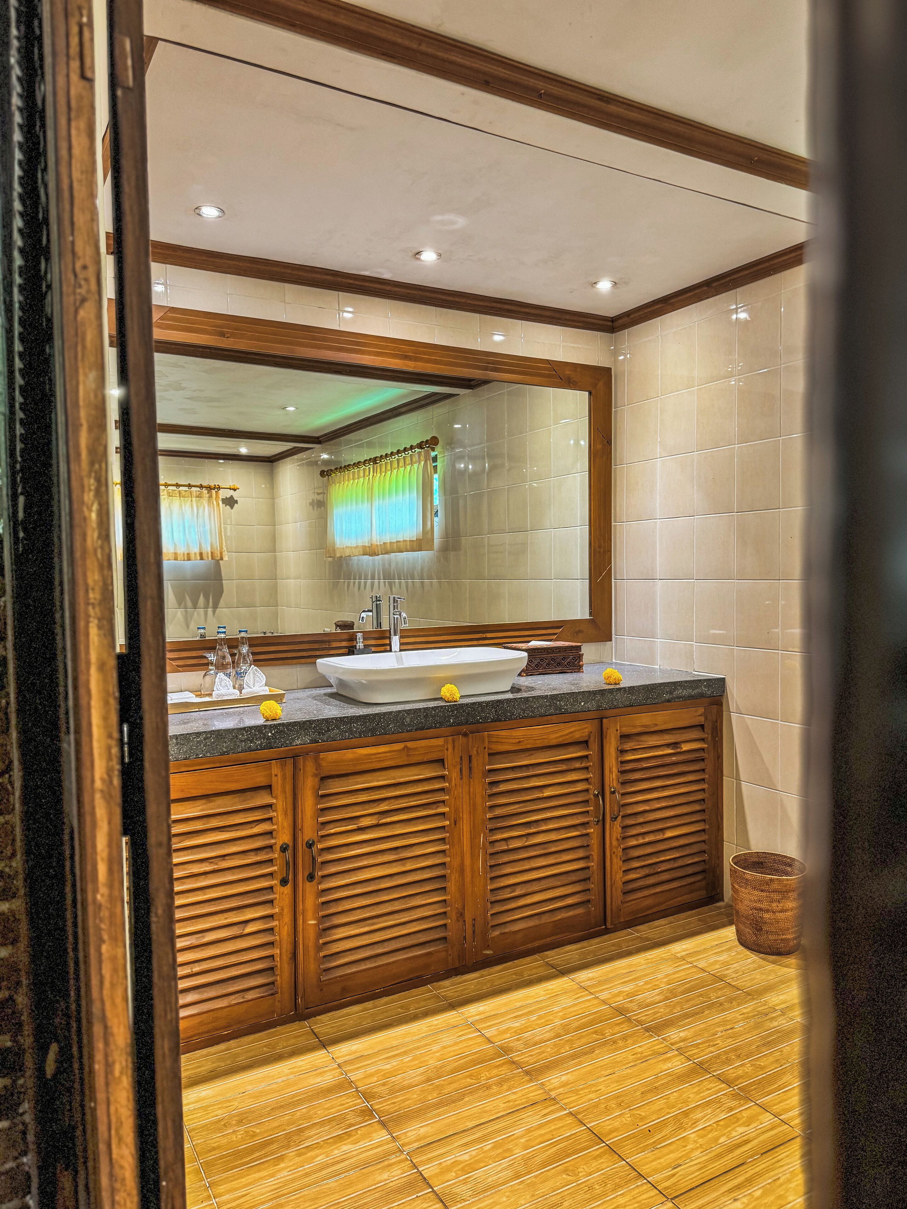 Un baño con un espejo grande, armarios de madera, un lavamanos y suelo de baldosas.