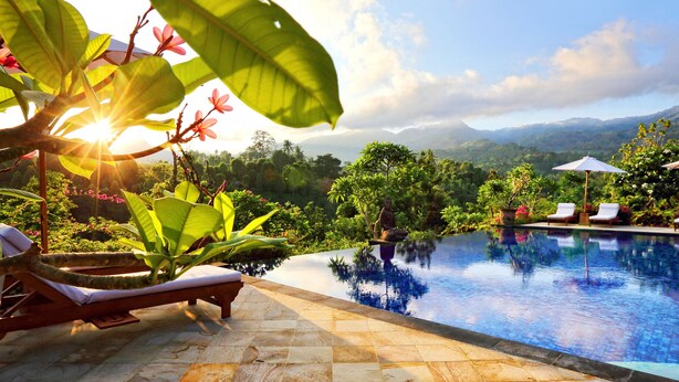 A poolside area with lounge chairs, a small table, and a view of mountains in the background. - Shanti Natural Panorama View Hotel (Sukasada)