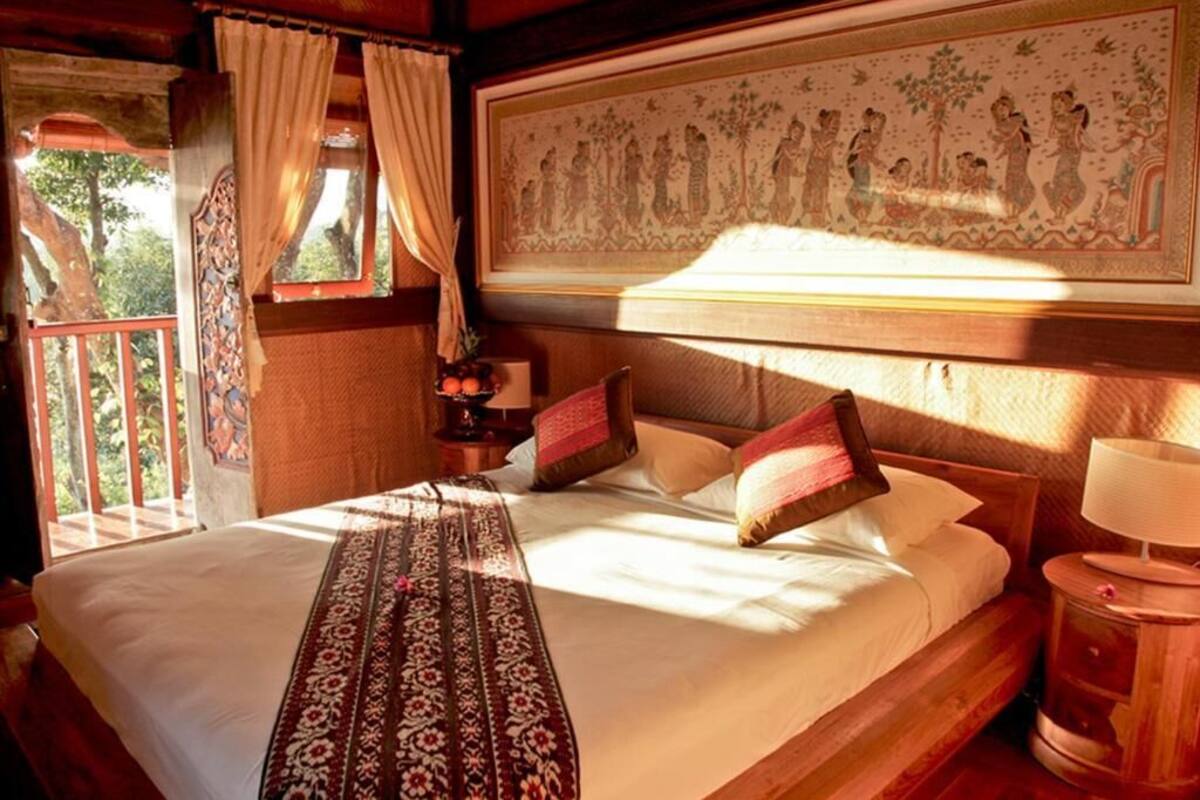 Ein hölzernes Bett mit einem gemusterten Überwurf, ein Nachttisch mit einer Lampe und ein großes gerahmtes Bild darüber.