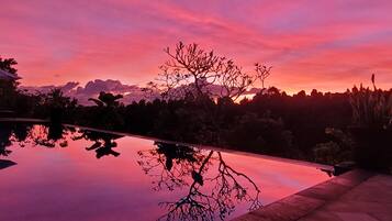 A serene sunset over a reflective pool with a tree silhouette and distant mountains.