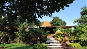 A traditional building with a tiled roof, surrounded by lush greenery and a stone pathway leading to the entrance. - Shanti Natural Panorama View Hotel (Sukasada)
