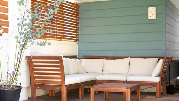 Un banco de madera y un sofá sobre una terraza de madera, con una pared verde al fondo.