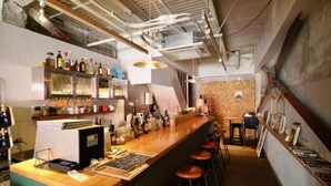 Un bar con mostrador de madera, taburetes y estantes llenos de botellas.