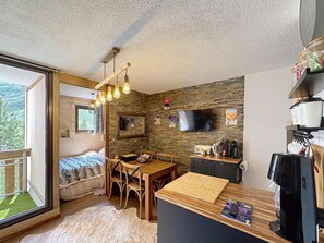 Ein kleines Zimmer mit Bett, Esstisch, Wandfernseher und einer Küchenzeile.