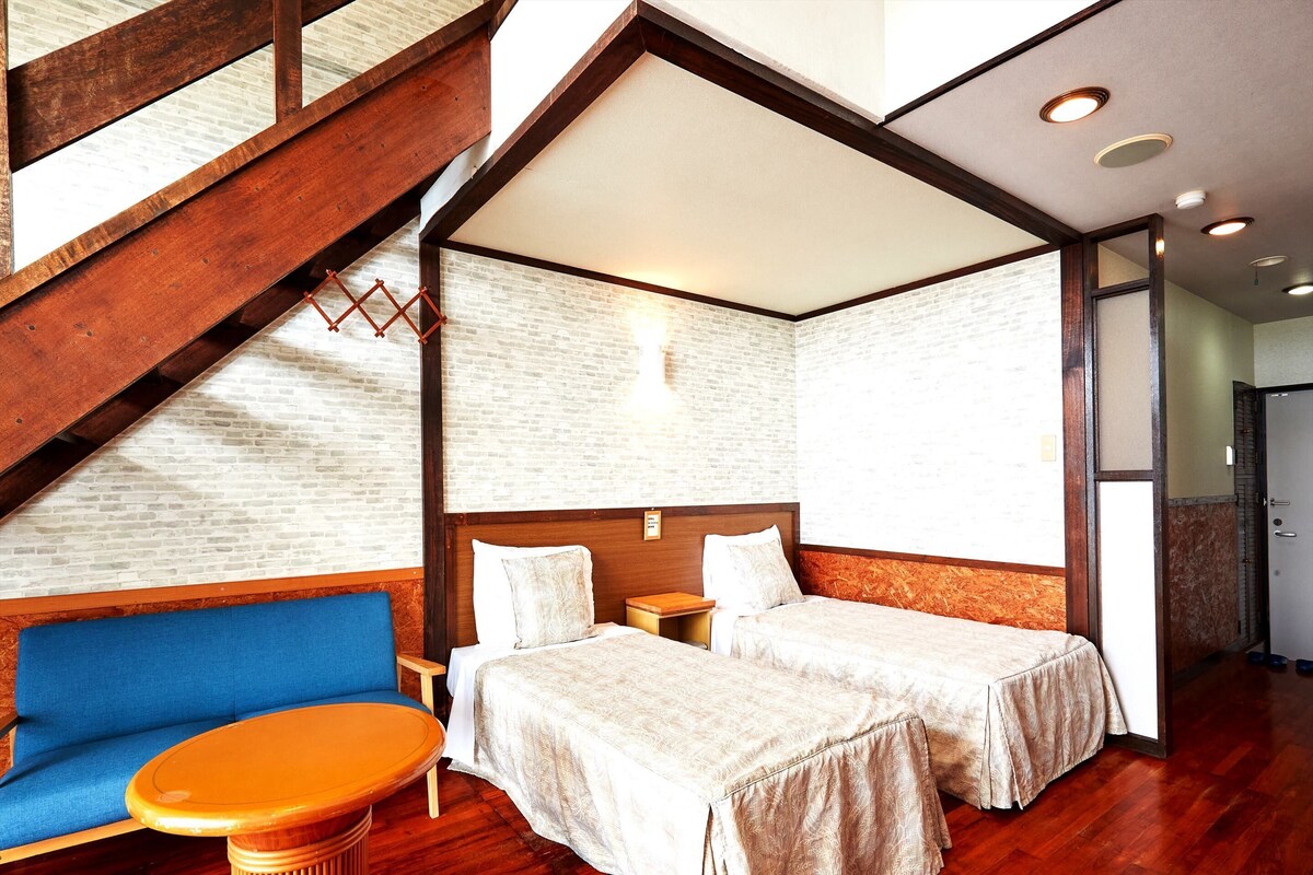 A hotel room with a loft-style design, featuring a wooden staircase, a loft bed, a blue sofa, and a wooden table.