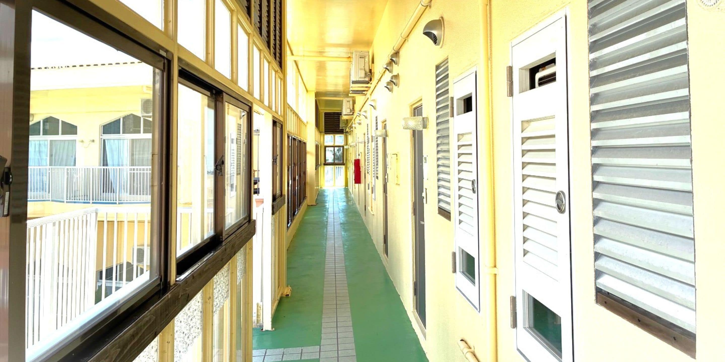 Um corredor com piso verde, portas brancas e janelas com persianas.