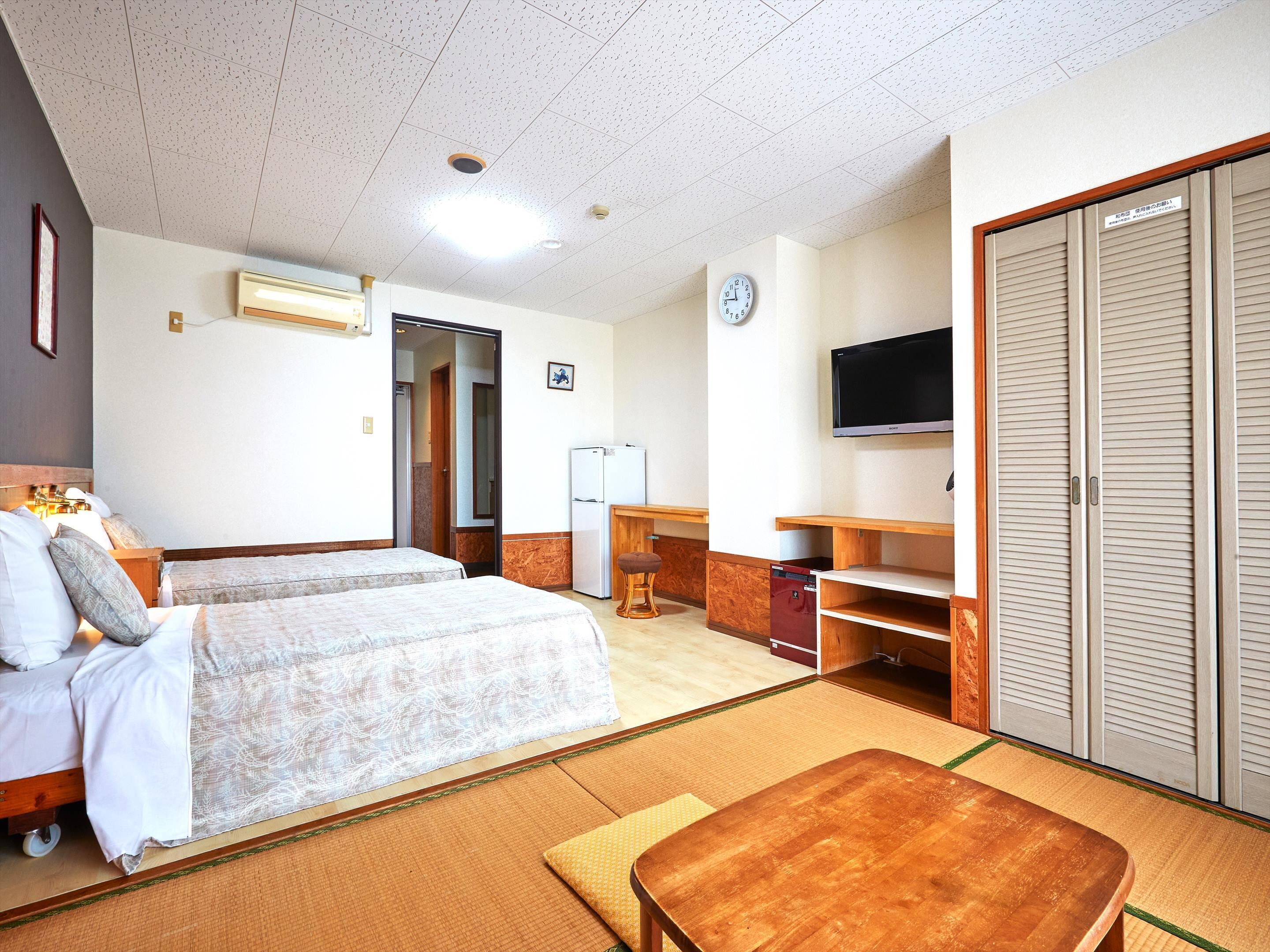 Ein Hotelzimmer mit zwei Betten, einem Fernseher, einem Kleiderschrank und einem kleinen Tisch.
