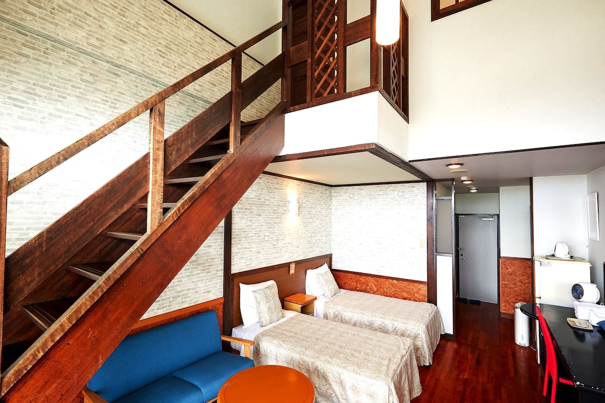 A hotel room with a wooden staircase, two beds, a blue sofa, and a small round table.