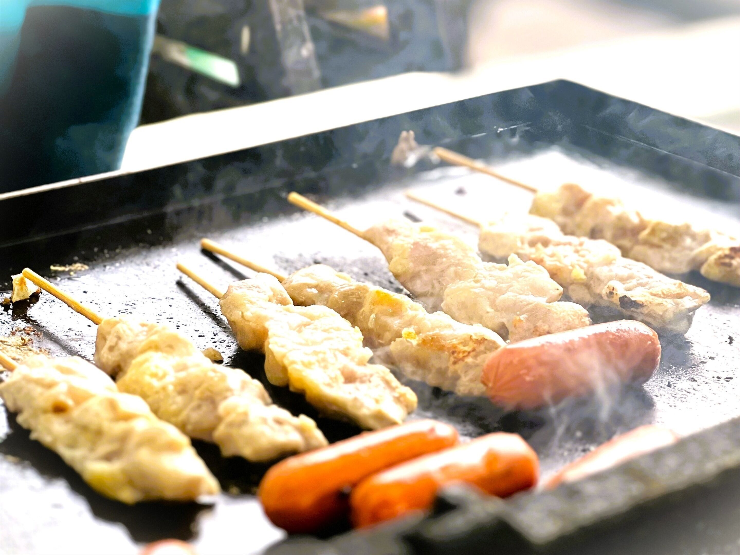 Skewers of meat and vegetables grilling on a flat surface.