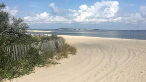 Une plage de sable bordée d’une clôture en bois et où la végétation est clairsemée.