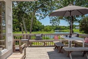 A wooden deck with a table and benches, overlooking a lake with trees and a house in the background. - Live on the Water: Dock, Beach, Boat, Kayak & Fish (Southampton)