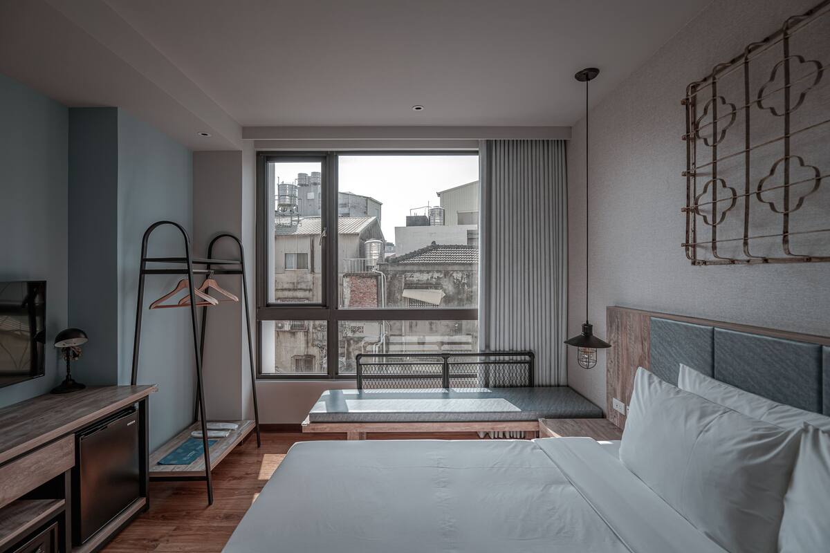 A modern hotel room with a large window, a bed, a desk, and a chair.