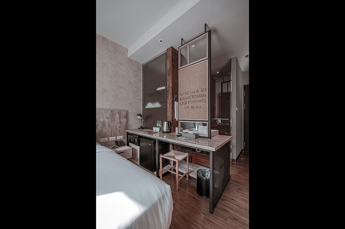 Een moderne hotelkamer met een bed, een klein bureau, een spiegel en een prullenbak.