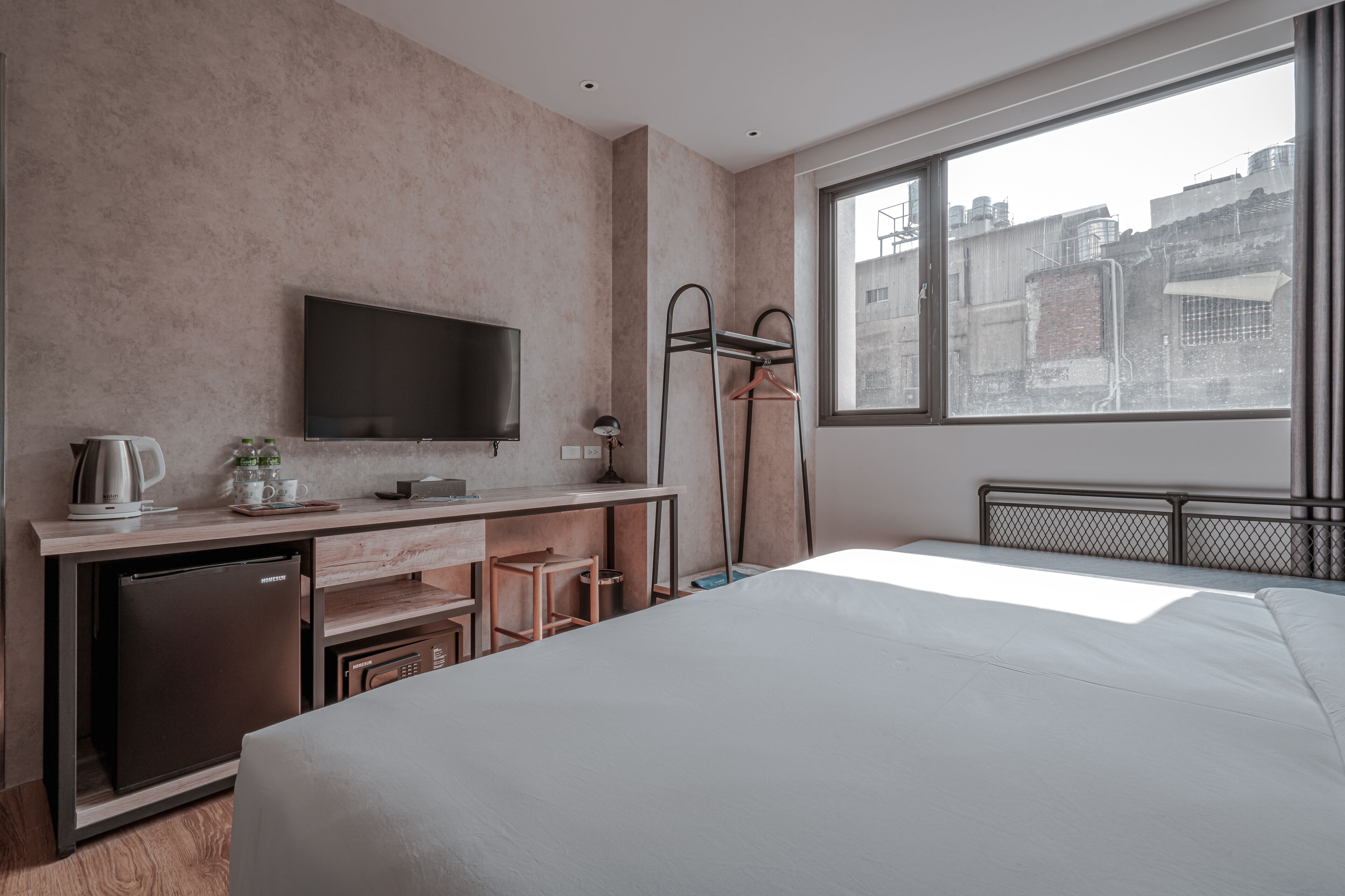 Une chambre d’hôtel équipée d’un lit, d’un bureau avec une télévision, d’une machine à café et offrant une vue sur les bâtiments à travers une grande fenêtre.